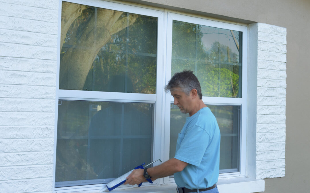 Homeowner caulking window with a caulk gun, an important part of weatherproofing homes and houses against rain, wind, hurricanes and storms.